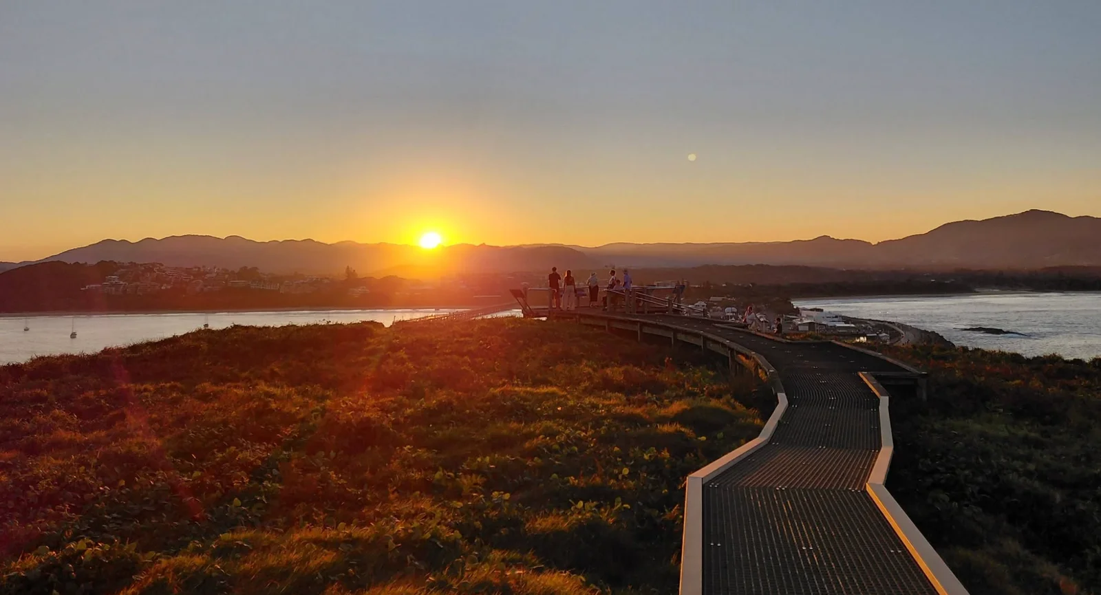 Sunset over the water and distant hills at Coffs Harbour, with a winding boardwalk in the foreground